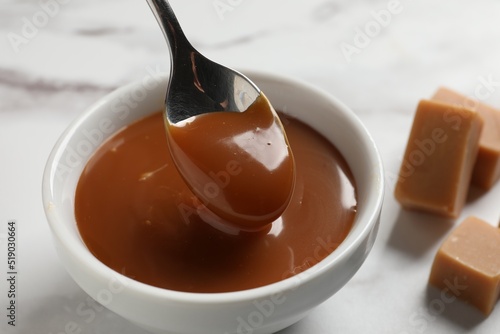 Taking yummy salted caramel with spoon from bowl on table  closeup