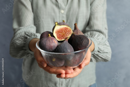 Woman holding glass bowl with tasty raw figs on light blue background, closeup