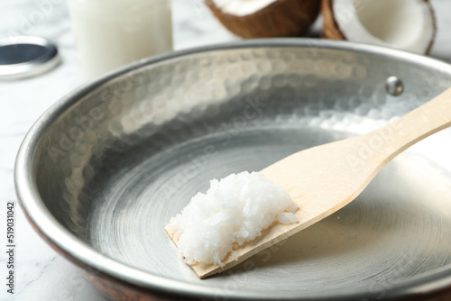 Frying pan with coconut oil and wooden spatula on white marble table, closeup. Healthy cooking