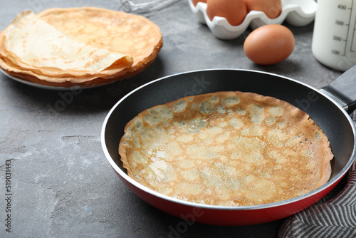 Delicious thin pancake in frying pan on grey table, closeup