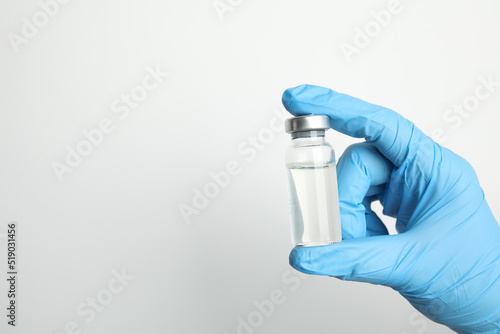 Doctor holding vial with medication on white background, closeup view and space for text. Vaccination and immunization