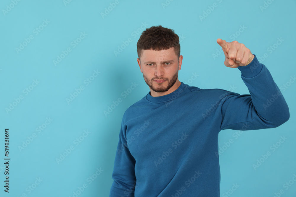 Aggressive young man pointing on light blue background. Space for text Aggressive young man pointing on light blue background. Space for text