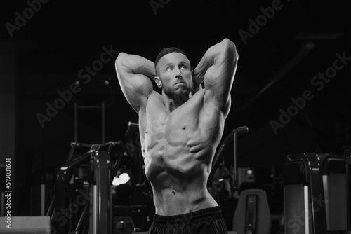 Obraz na płótnie A bodybuilder with a beard is doing a stomach vacuum pose after a workout in a gym. w salonie