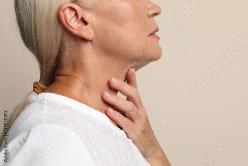Mature woman doing thyroid self examination on beige background closeup photo