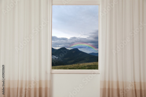 View of beautiful rainbow in mountains through window