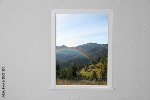 View of beautiful rainbow in mountains through window