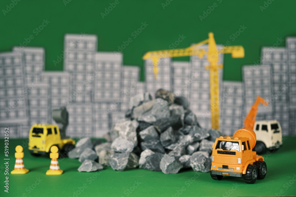 Obraz premium Models simulator on green background, construction vehicles toys, trucks, backhoes, and cranes work at site, transport resource materials, rock, and mortar, real estate business, and city development.