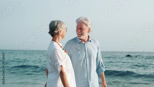 Couple of old mature people walking on the sand together and having fun on the sand of the beach enjoying and living the moment. Two cute seniors in love having fun. Barefoot walking on the water
