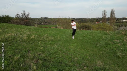 Aerial View of Young Man Doing Somersault Roll and Running in Green Outdoor Field, Slow Motion Drone Shot photo