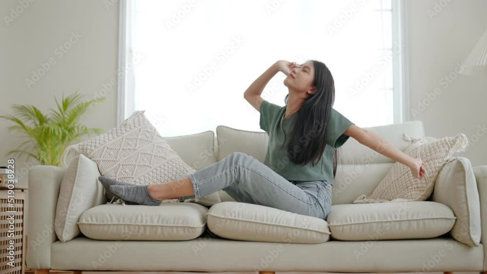Young asian woman using mobile smart phone and lying down on couch. Female wake up on sofa and body stretching and feeling fresh Young asian woman using mobile smart phone and lying down on couch. Female wake up on sofa and body stretching and feeling fresh