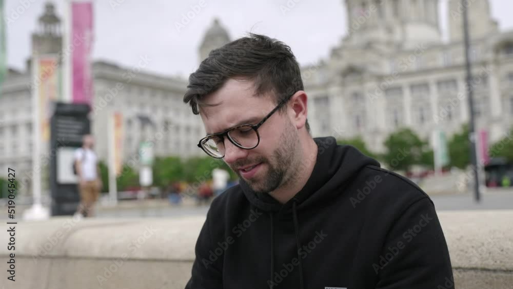Young mid-twenties white male smiling using mobile phone answering call in left hand in cinematic slow motion. Mid-tight shot showing Liverpool in background. Young mid-twenties white male smiling using mobile phone answering call in left hand in cinematic slow motion. Mid-tight shot showing Liverpool in background.
