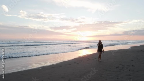 Young woman walking back from the warm south pacific ocean with a magnificent sunset in the background. Wide angle pull back shot photo