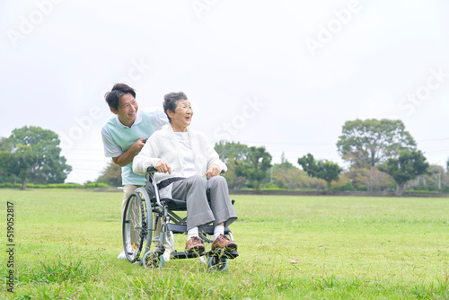 車椅子に乗って散歩する高齢者女性と介護士