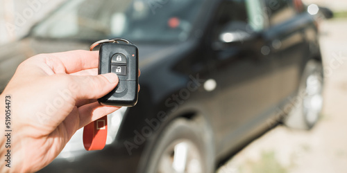 Hand pushing remote control button to unlock car alarm outdoors. Close-up, banner with copy space
