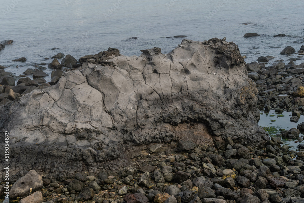 Large volcanic rock formation on island coast with ocean water in background.