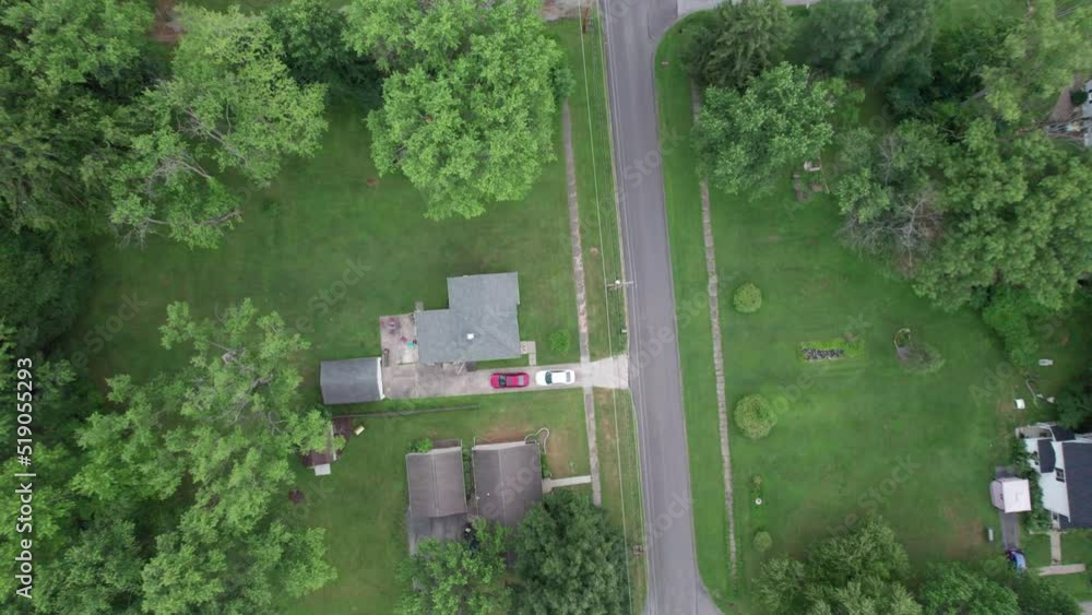 Aerial drone landing shot over a residential houses surrounded by lush green vegetation by the side of a road at daytime. Aerial drone landing shot over a residential houses surrounded by lush green vegetation by the side of a road at daytime.