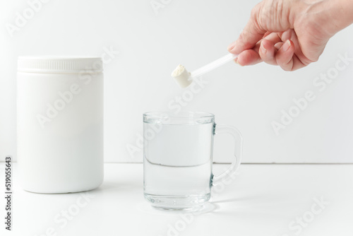 Woman pouring bovine colostrum powder into glass of water photo