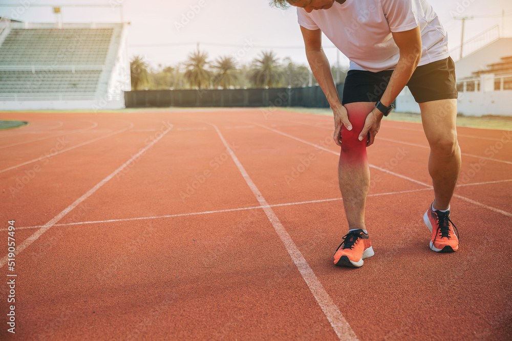 Runner man with sports running knee injury at racetrack. Hands holding knee with painful (ankle knee twist).