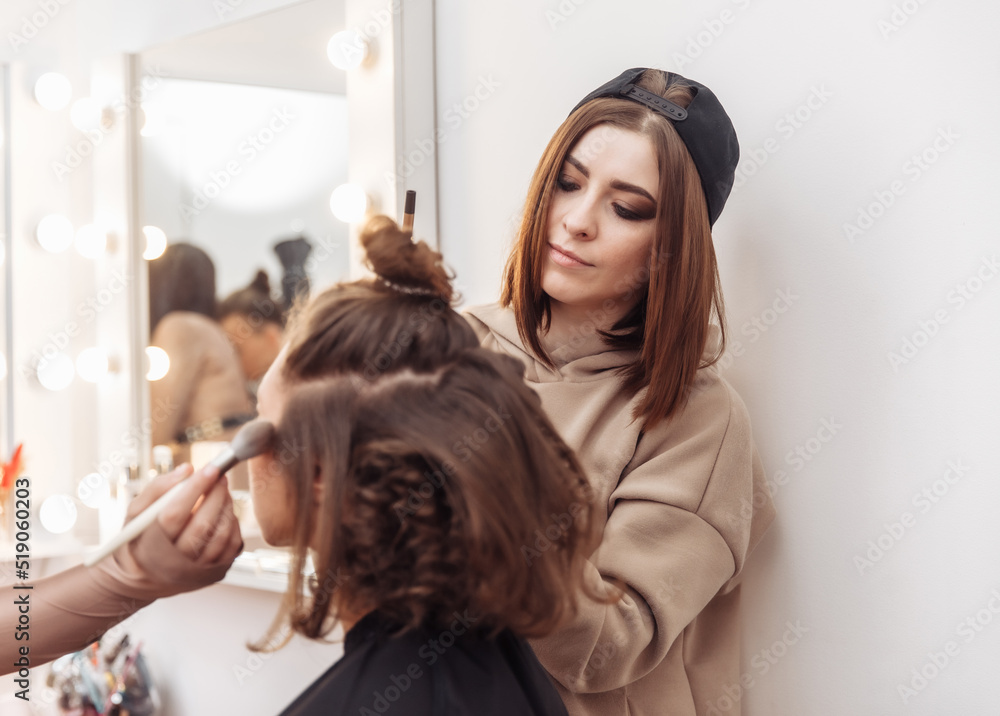 Fototapeta premium Professional make-up and hair style artists doing make-up and hair curls to a beautiful caucasian woman in a beauty salon