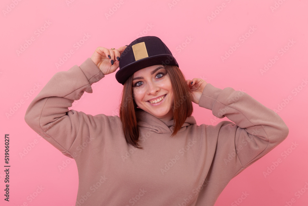 Young swag style woman in cap and hoodie posing on pink background. Young swag style woman in cap and hoodie posing on pink background.