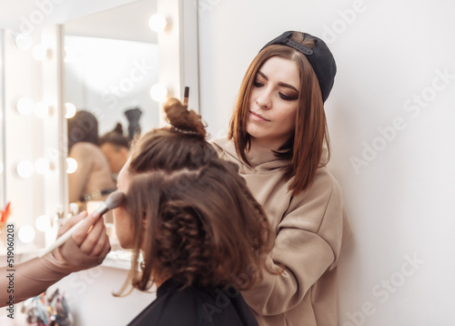 Professional make-up and hair style artists doing make-up and hair curls to a beautiful caucasian woman in a beauty salon