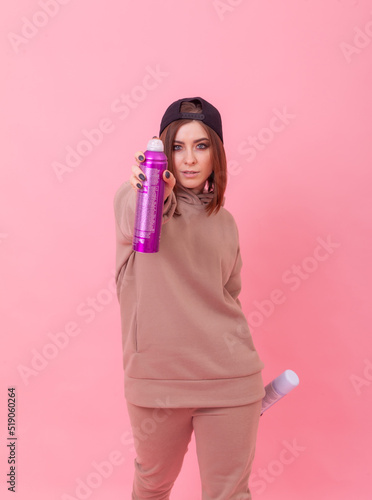 Portrait of a hair stylist with sprays of hairspray on a pink background. Young beautiful woman in cap and hoodie