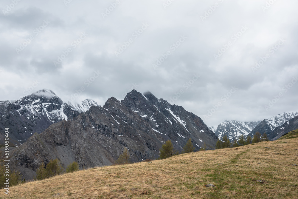 Atmospheric landscape with large thorny dragon shaped mountain top under gray cloudy sky. Gloomy top view from hill to high snowy mountain range with sharp rocks in shape of dragon back in low clouds.