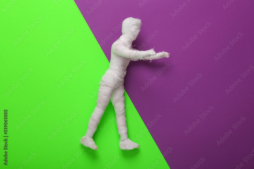 Mummy doll wrapped in bandages on a green-violet background. Halloween minimal still life. Top view Mummy doll wrapped in bandages on a green-violet background. Halloween minimal still life. Top view