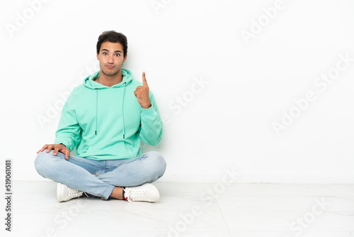 Caucasian handsome man sitting on the floor pointing with the index finger a great idea