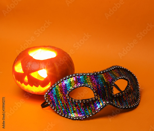 Halloween pumpkin head jack lantern with burning candles and carnival mask on orange background