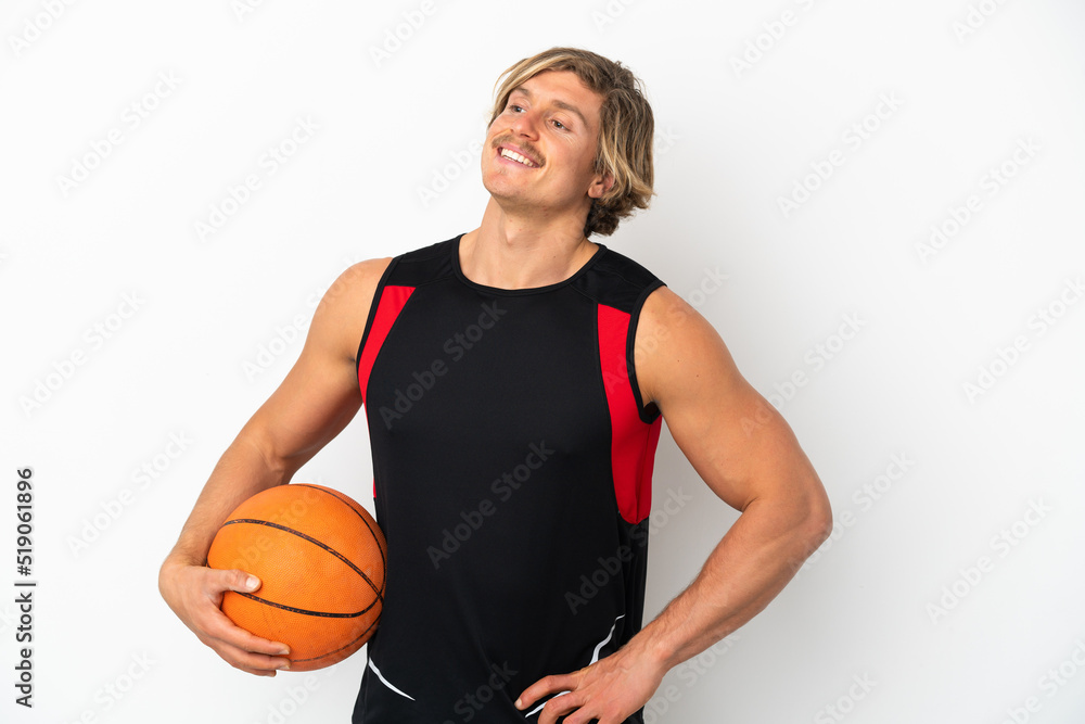 Young blonde man holding a ball of basketball isolated on white background posing with arms at hip and smiling