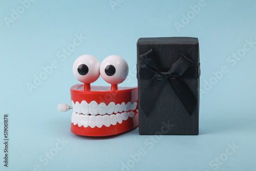 Quadro em tela Funny toy clockwork jumping teeth with eyes and gift box on blue background