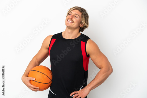 Young blonde man holding a ball of basketball isolated on white background posing with arms at hip and smiling