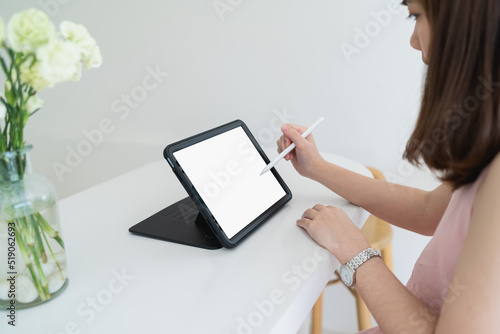 Artist woman hand holding a stylus pen while using a digital tablet with white blank screen in the coffee shop. Young creative woman holding stylus pen and working with tablet. photo