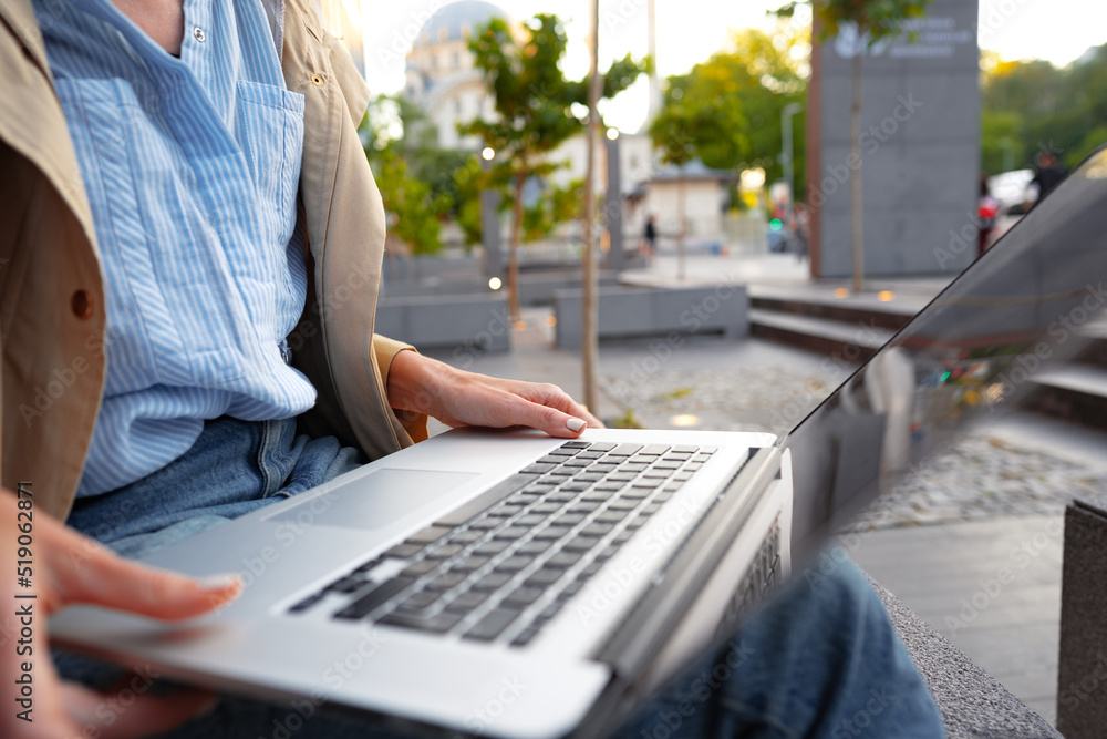 Close up of female hands typing on computer keyboard of a laptop sitting in the street Close up of female hands typing on computer keyboard of a laptop sitting in the street