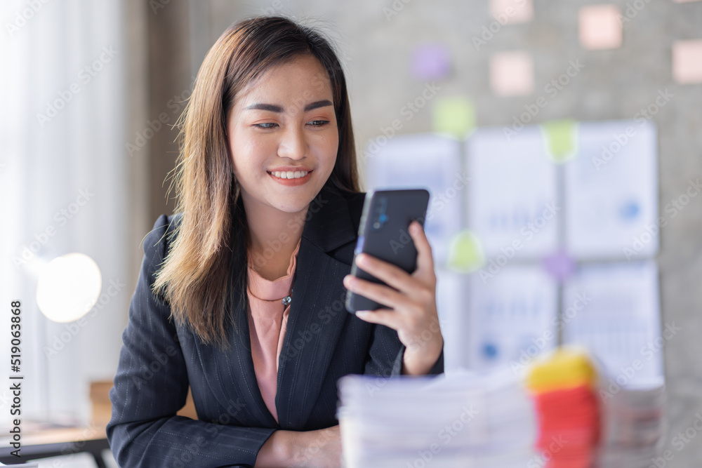 Business asian woman using mobile phone during checking an email or social media on internet working on laptop accounting financial concept. Business asian woman using mobile phone during checking an email or social media on internet working on laptop accounting financial concept.
