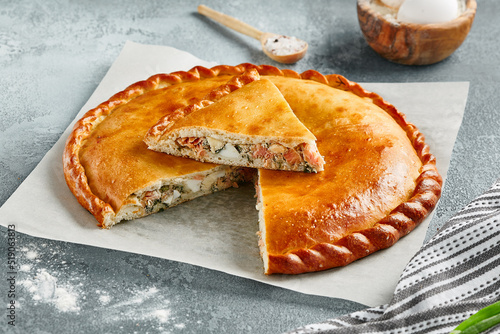 Classic pie with salmon and white fish on wooden board. Composition with fish pie on concrete background with textile and spices. Homemade pie with fish in rustic style on gray table.