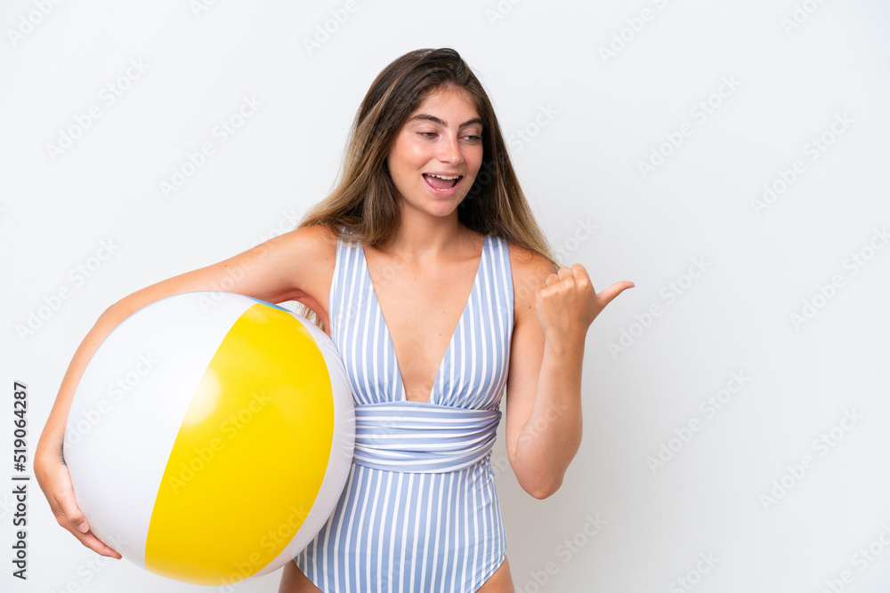 Young woman in swimsuit holding beach ball isolated on white background pointing to the side to present a product Young woman in swimsuit holding beach ball isolated on white background pointing to the side to present a product
