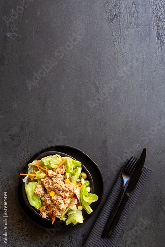 Healthy fitness salad bowl with tuna, lettuce, tomatoes and other vegetables on black background .Copy space
