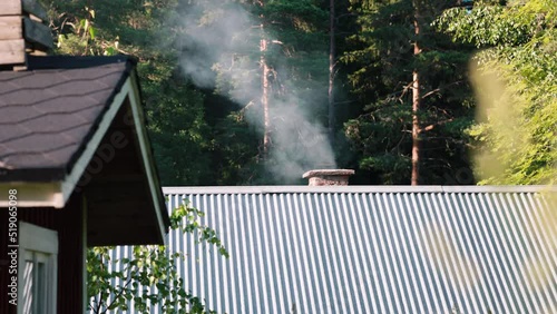 smoke wafts out of a chimney in a mountain resort.  A bit of green wood makes for a bit of extra smoke in this cinematic shot.  Tall blades of seeding grass move into the foreground photo