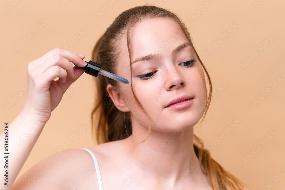 Young caucasian girl isolated on beige background holding a serum. Close up portrait