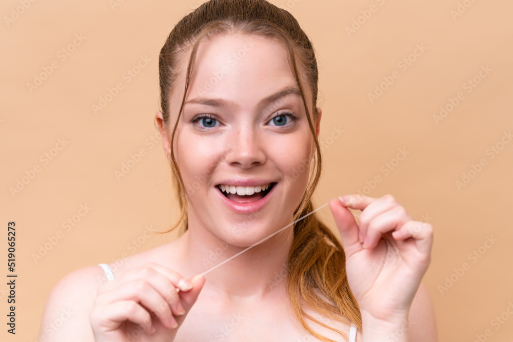 Young caucasian girl isolated on beige background with dental floss. Close up portrait