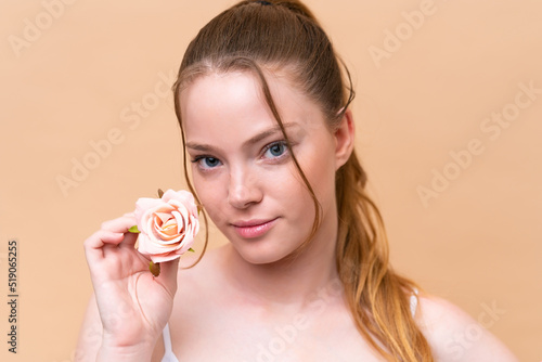 Young caucasian girl isolated on beige background holding flowers. Close up portrait