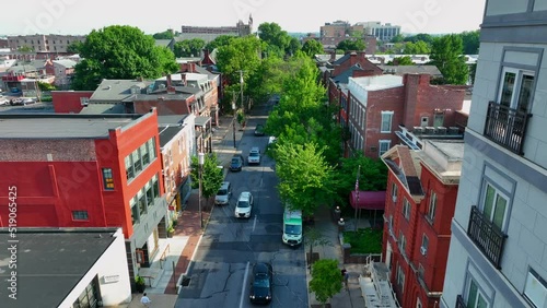 Cars drive down busy one-way street in small American city. Tree lined sidewalks make city walkable while transportation by car remains accessible. photo