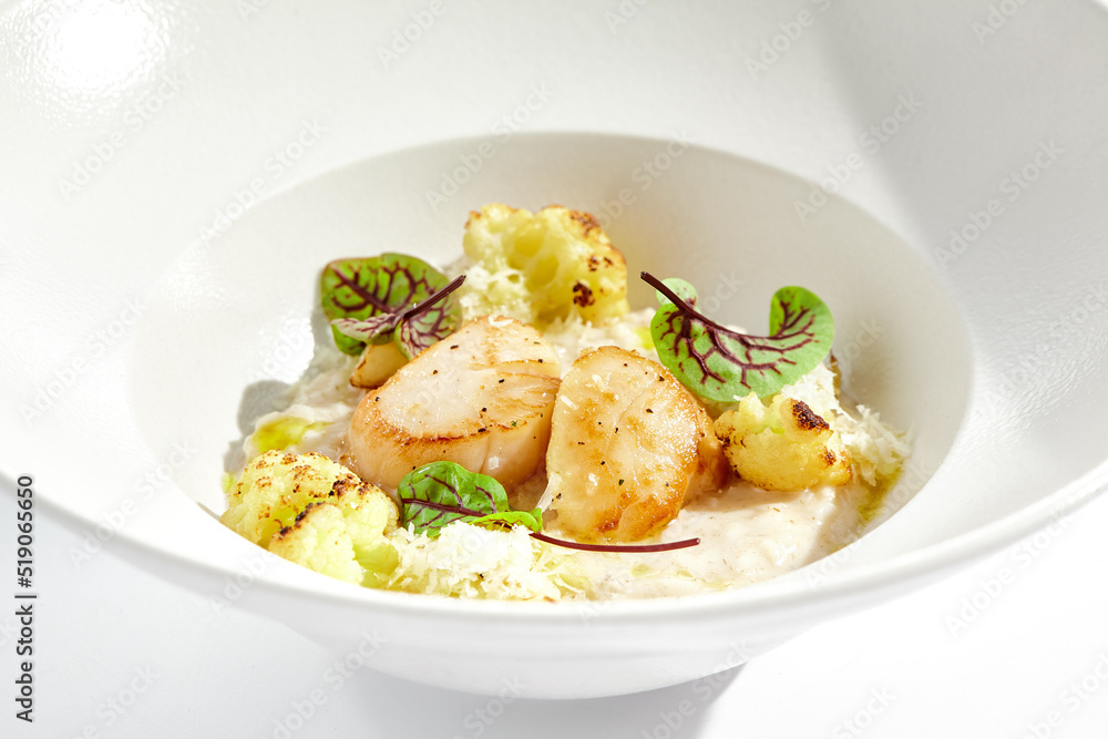 Delicious creamy risotto with sea scallop and cauliflower. Elegant main course with seafood on white plate. Grilled scallop with cauliflower and creamy rice. Seafood risotto with scallops.