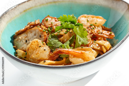 Pan asian food - udon with prawn, chicken wok on white background. Noodle with chicken and prawn in ceramic bowl. Indonesian wok with udon noodles. Spicy thai dish from noodle with shrimp and chicken.