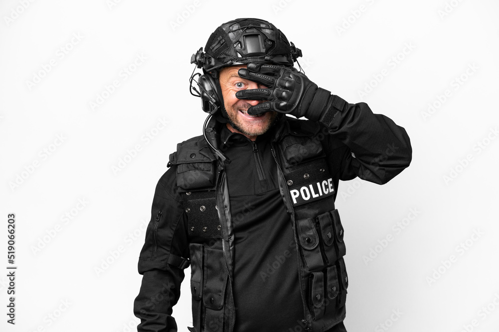 Middle age SWAT man isolated on white background covering eyes by hands and smiling Middle age SWAT man isolated on white background covering eyes by hands and smiling
