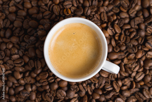 Small white coffee cup with espresso crema on roasted beans background. Selective focus