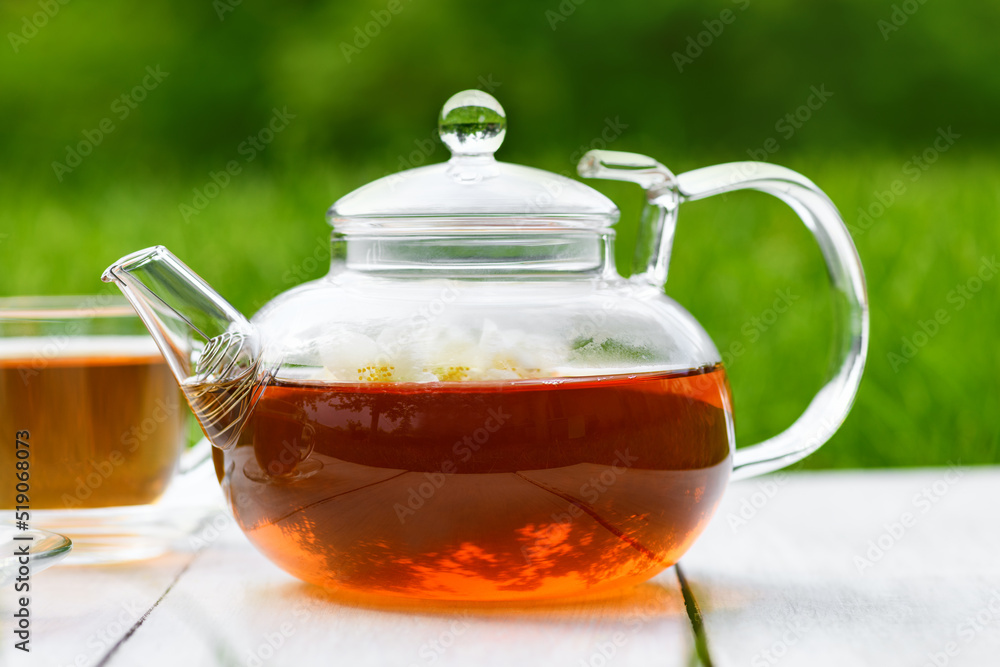 Jasmine tea and flowers in glass teapot on a wooden white background. Teapot with green jasmine tea on a green background Jasmine tea and flowers in glass teapot on a wooden white background. Teapot with green jasmine tea on a green background