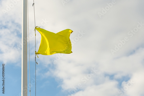 Yellow small flag on flagpole with cloudy sky.